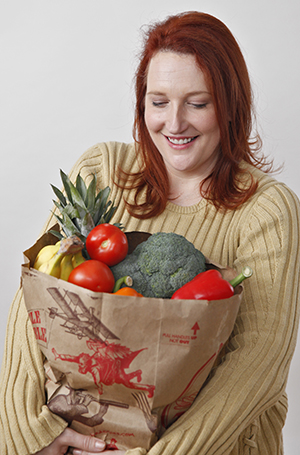 Una mujer sostiene una bolsa de compras llena de frutas y verduras.