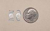 Lentes intraocular junto a una moneda de 10 centavos para comparar el tamaño.