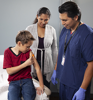 Proveedor de atención médica aplicando un inyección en el brazo a un niño mientras una mujer mira.